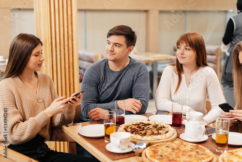 A group of friends is having pizza in a cozy restaurant and taking selfies  taking pictures together. A cheerful group of friends.