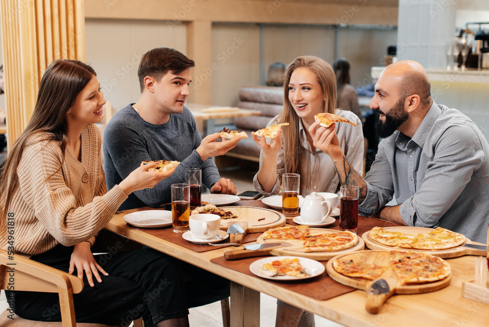 A cheerful group of friends is eating delicious pizza in a restaurant. Friends are sitting in a restaurant and having fun.