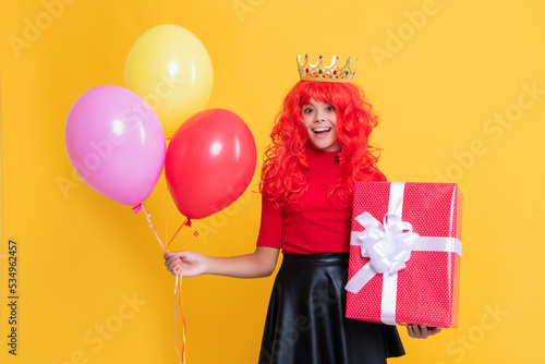 happy surprised kid in crown with present box and party balloon on yellow background