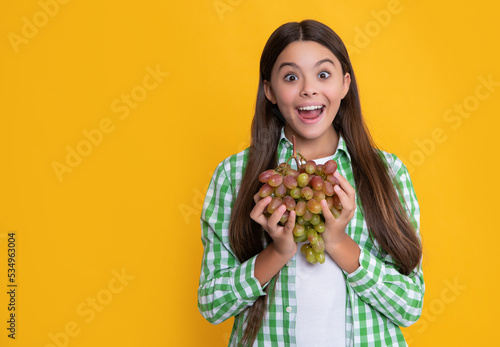 shocked child with grapes bunch on yellow background. vitamins