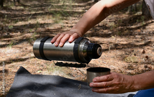 women's hands pour tea from a thermos in the forest on a picnic