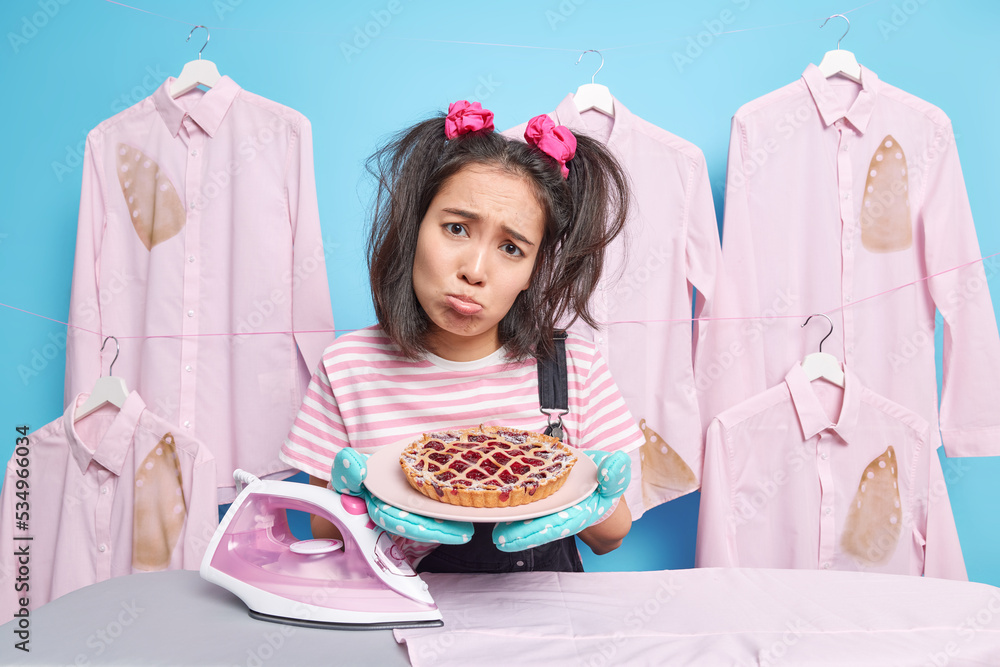 Dissatisfied Asian woman has sulking face expression purses lips holds