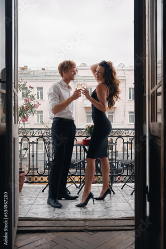 Beautiful young couple embracing and toasting with champagne while standing on the balcony together