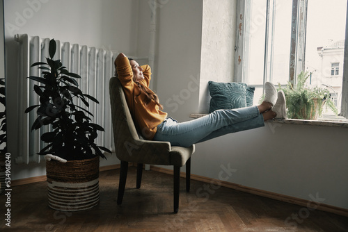 Obraz na plátně Beautiful young woman holding hands behind head while relaxing on the chair at h