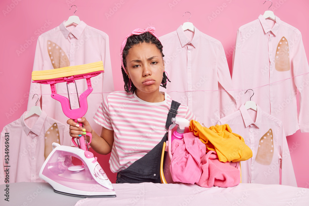 Φωτογραφία Upset tired housewife feels exhausted after doing washing and ironing has much work about house holds mop and basket full of laundry stands near board dressed in casual clothes