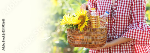Woman holding basket with bottles of oil and sunflowers in field. Banner for design