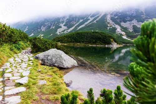 Fototapeta Naklejka Na Ścianę i Meble -  A very impressive view of the Polish Tatra mountains with many rocks with a incredibly beautiful turquoise lake in the middle of mountains with the reflection of white clouds and mountains