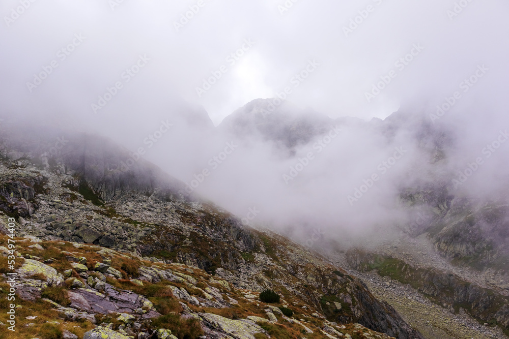 Impressive landscape with large grey-brown mountains in the Polish Tartars with a rocky hiking path in the white fog and clouds