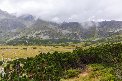 Very beautiful landscape in the Polish Tatras with huge gray mountains that reach the white clouds and a natural turquoise lake in the middle 