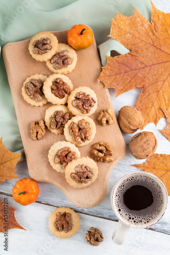 On the table is a wooden board with cookies and nuts and a cup of coffee and autumn maple leaves.