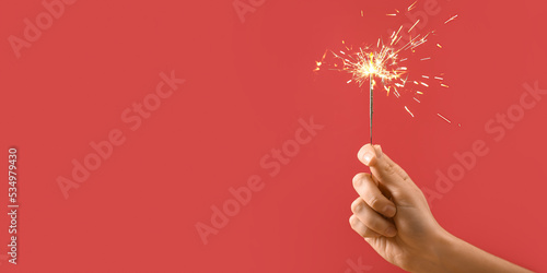 Female hand holding Christmas sparkler on red background with space for text