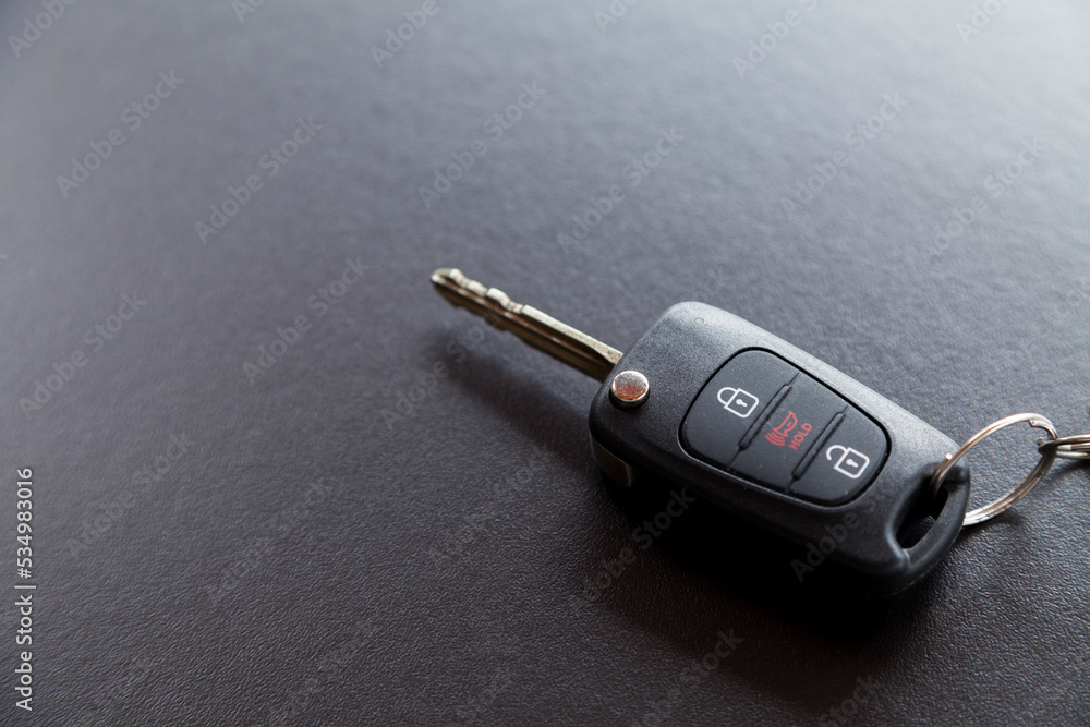 Car key on top of a black table with natural light. Key with buttons to lock and unlock the door. Car key concept. Door lock concept. Copy space. Car key on top of a black table with natural light. Key with buttons to lock and unlock the door. Car key concept. Door lock concept. Copy space.