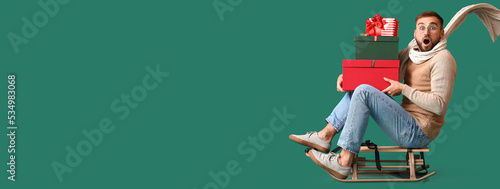 Fotografie Emotional man with Christmas gifts sitting on sledges against green background w