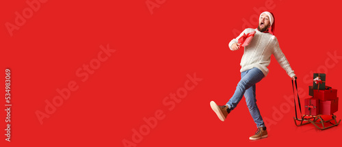 Walking man with heap of Christmas gifts on sledges against red background with space for text