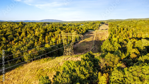Transmission tower or electricity pylon with overhead power lines and path cut through a forest