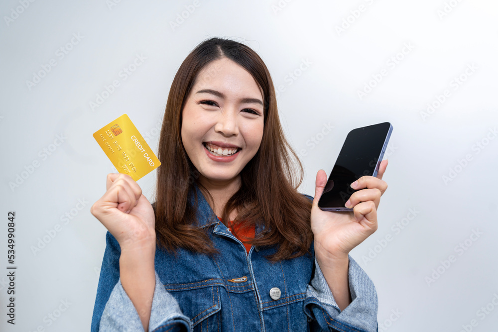 Portrait of an Asian woman in Thailand wearing a blue jeans and an orange T-shirt. Enjoy using your credit card on your mobile phone. isolated white background Portrait of an Asian woman in Thailand wearing a blue jeans and an orange T-shirt. Enjoy using your credit card on your mobile phone. isolated white background