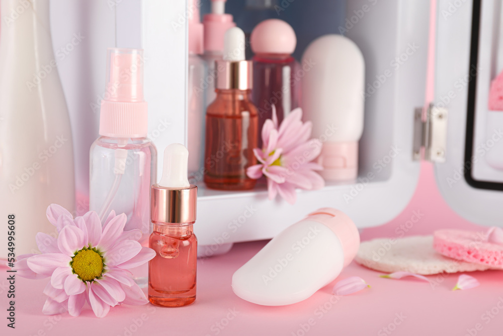 Small refrigerator with cosmetic products and flowers on pink background, closeup Small refrigerator with cosmetic products and flowers on pink background, closeup