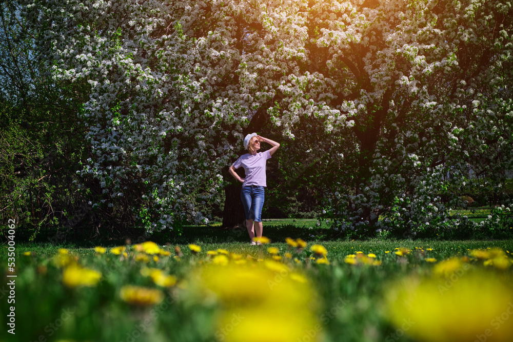 View from afar happy woman in spring blooming park. Female hipster enjoying beautiful nature in sunny day. Broad plan, selective soft focus. View from afar happy woman in spring blooming park. Female hipster enjoying beautiful nature in sunny day. Broad plan, selective soft focus.