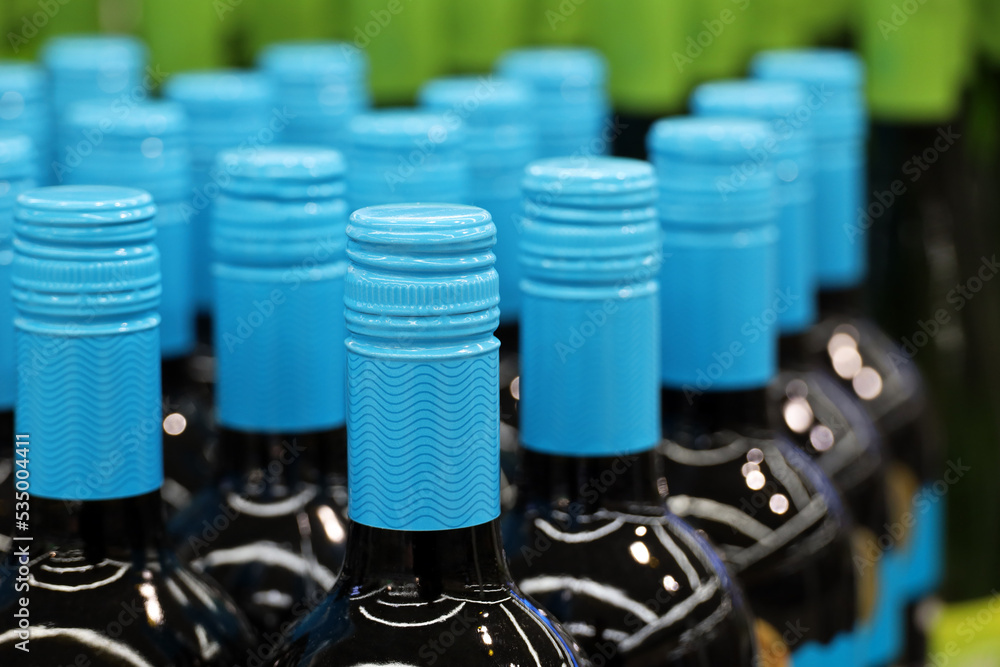 Wine bottles with blue lids in a row. Liquor store, red wine production concept Wine bottles with blue lids in a row. Liquor store, red wine production concept