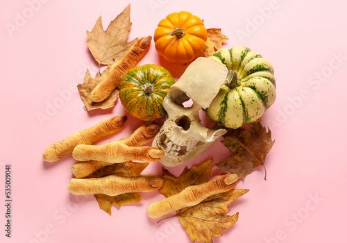 Witch finger cookies with human skull, pumpkins and fallen leaves on pink background