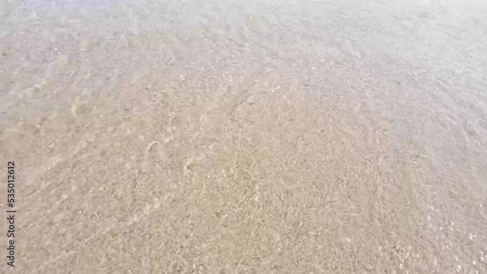 Small waves of sea water moving back and forth to the beach sand. Sea waves move gently on the beach sand with soft foam foam during summer vacation Small waves of sea water moving back and forth to the beach sand. Sea waves move gently on the beach sand with soft foam foam during summer vacation