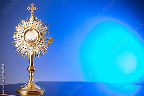 Catholic religion concept. Catholic symbols composition. The Cross, monstrance,  Holy Bible and golden chalice on blue bokeh background. 