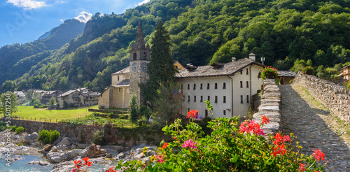 Lillianes, Aosta Valley. Italy. View of the stone bridge over the Lys stream and the Church of San Rocco. Some flowers in foreground. July 27, 2022. photo