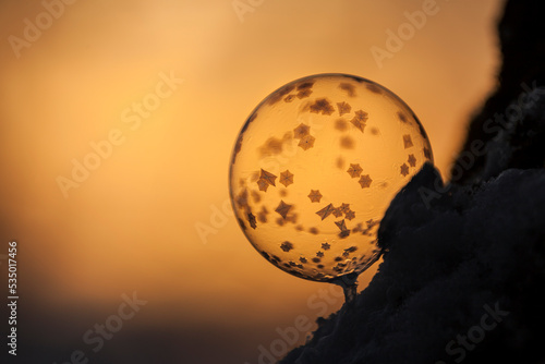 Close-up of frozen bubble against sky during sunset in orange light with small crystals