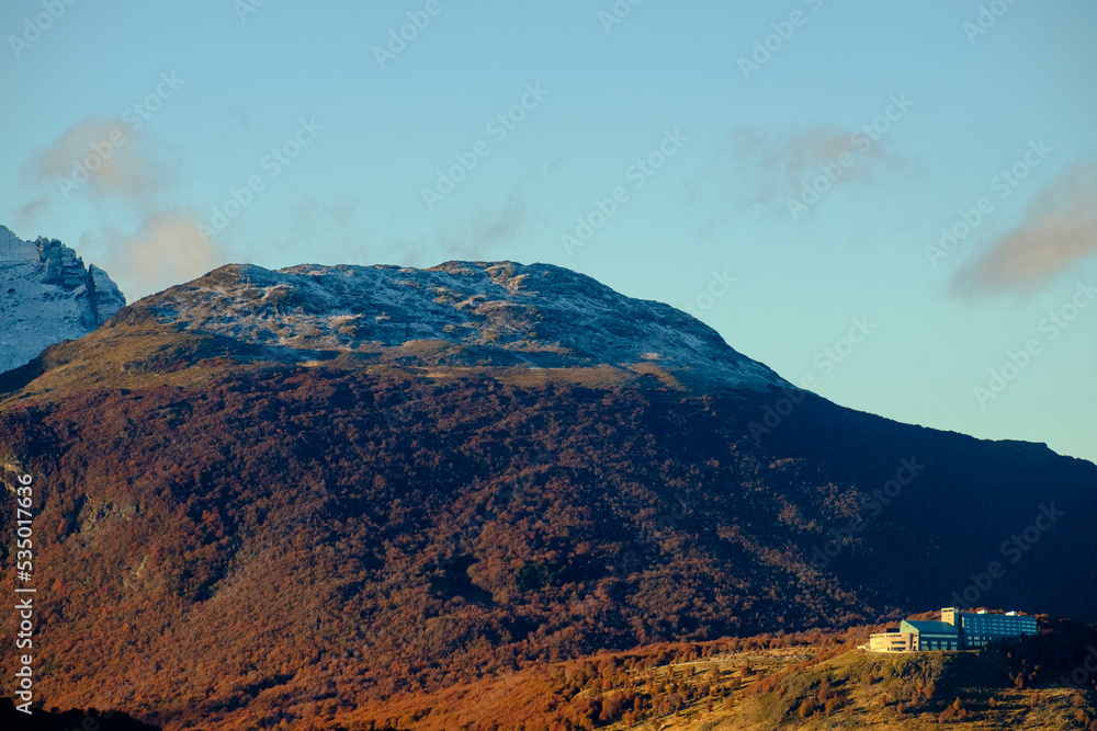 Obraz premium Lonely hotel on a hill looking down on Ushuaia, Argentina. Late sunlight enlightens the autumn forest.