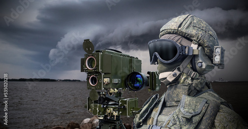 Navy soldier. Laser rangefinder next to soldier. Man in camouflage military uniform. Equipment for naval army. Soldier stands on bank of river. Military technologies. Warrior in face mask and helmet