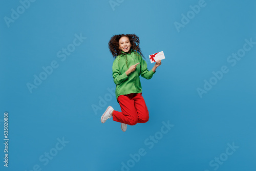 Full body young woman of African American ethnicity 20s she wear green shirt jump high hold gift certificate coupon voucher card for store isolated on plain blue background. People lifestyle concept.