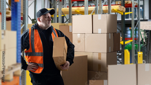 Man inside warehouse. Businessman with boxes. Guy in orange reflective vest. Businessman in warehouse with products. Owner of company is engaged in warehouse work. Businessman among storage racks photo