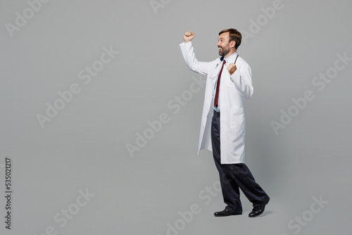 Side view full body happy fun male doctor man wears white medical gown suit work in hospital doing winner gesture isolated on plain grey color background studio portrait. Healthcare medicine concept.