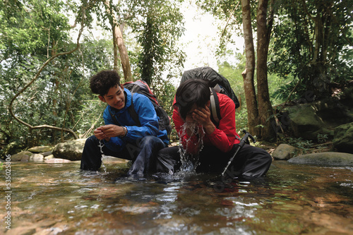 Two young trekkers or traveler sits on rocks in mountain river and enjoy splashing natural water in hands for washing his face with mountain stream water. Refresh himself after a long journey.