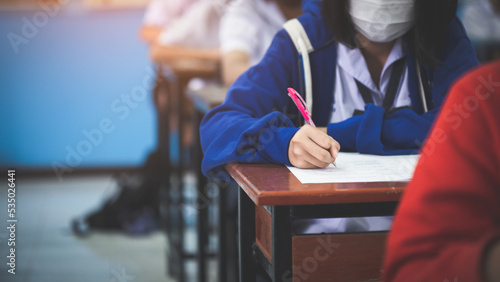 Student taking exam while wearing face mask due to coronavirus emergency. Young woman sitting in class with wearing surgical mask due to Covid-19 pandemic.