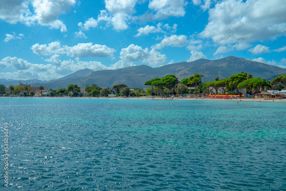 Blick über das türkisblaue Meer auf den Strand von Mondello mit seinen Bergen im Hintergrund und blauem Himmel mit vielen kleinen Wolken.