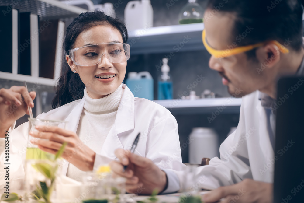 Researcher woman are mixing liquid in the beaker and researcher man are look to substance and notes on a pen to notebook in his hand at laboratory. Researcher woman are mixing liquid in the beaker and researcher man are look to substance and notes on a pen to notebook in his hand at laboratory.
