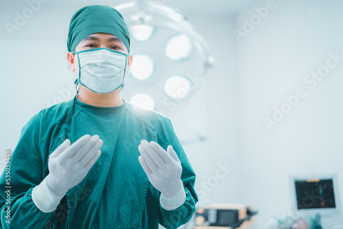 Portrait confidence doctor wear protective suit with glove,medical mask, stand in operate theater room with patient in background. Professional surgeons. Healthcare, Hospital emergency medical concept