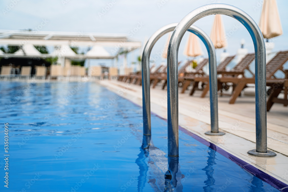 close up of grab bars outdoor swimming pool entrance with sunlounger chairs terrace in the background close up of grab bars outdoor swimming pool entrance with sunlounger chairs terrace in the background