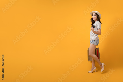 Beautiful Asian shopaholic woman smiles and happy while carrying shopping bags and credit card on yellow background. Summer sale, Mid-year sales concept. photo