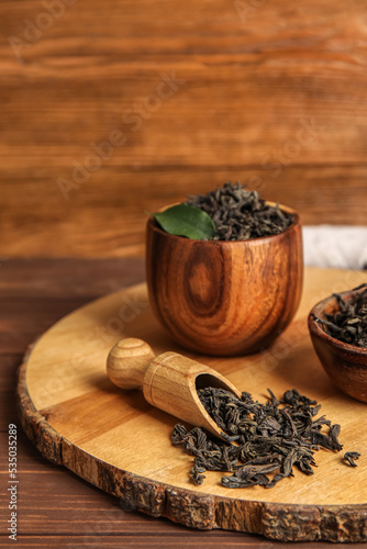 Bowl and scoop with dry tea leaves on wooden background