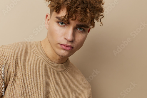 close horizontal portrait of a handsome, charming man with curly hair standing in a beige sweater on a beige background