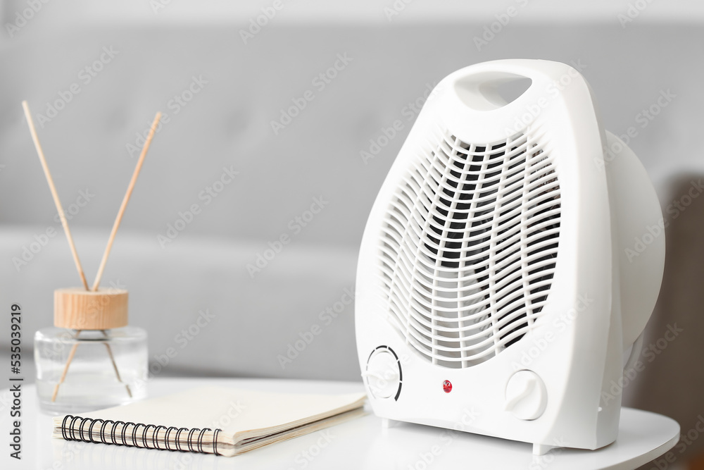 Electric fan heater, notebook and reed diffuser on table in living room ...