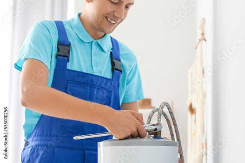 Male plumber repairing boiler with wrench in bathroom