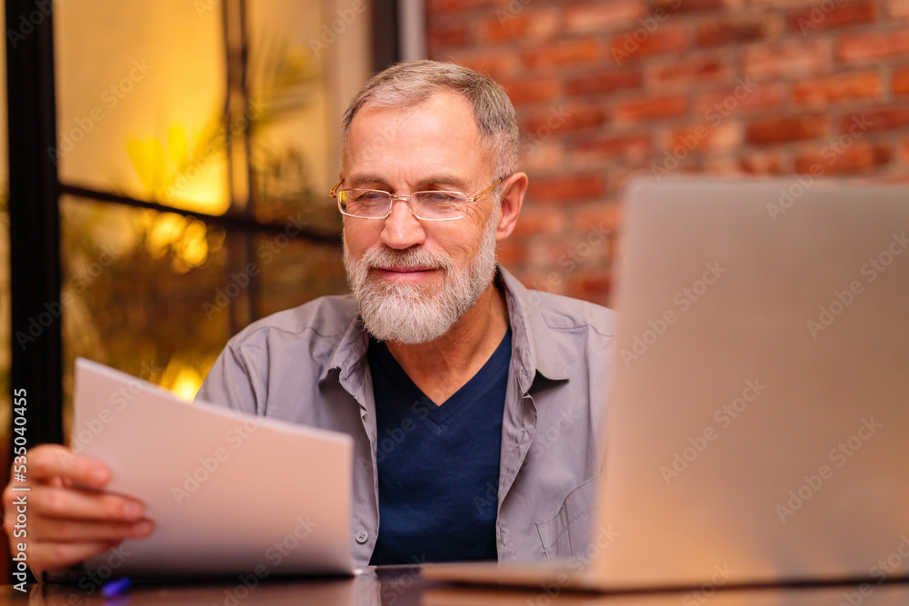 Smiling senior middle aged man in glasses working on laptop at home Smiling senior middle aged man in glasses working on laptop at home