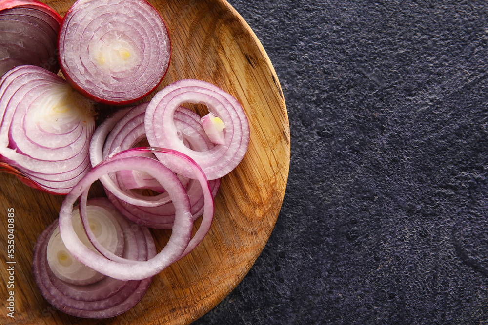 Wooden plate with cut red onion on dark background, closeup Wooden plate with cut red onion on dark background, closeup