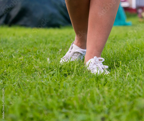 women's feet in white sneakers on the grass on the lawn
