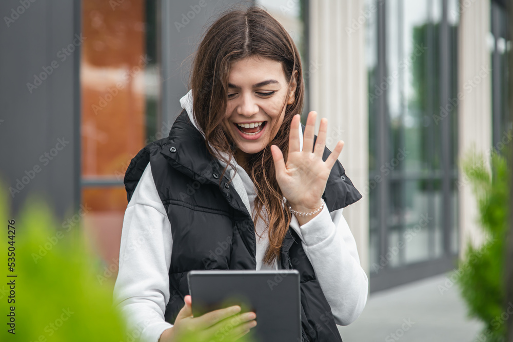 Attractive young woman uses a tablet, communicates by video call outside. Attractive young woman uses a tablet, communicates by video call outside.