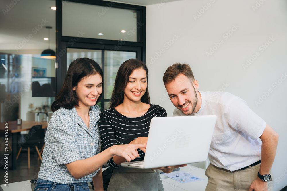 Diverse, ecstatic businesspeople discussing papers and working on laptops at an office table while smiling. Diverse, ecstatic businesspeople discussing papers and working on laptops at an office table while smiling.