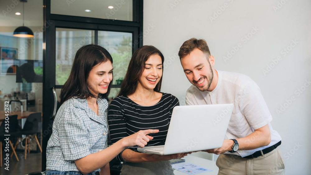 Diverse, ecstatic businesspeople discussing papers and working on laptops at an office table while smiling. Diverse, ecstatic businesspeople discussing papers and working on laptops at an office table while smiling.
